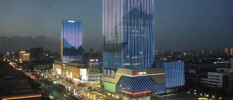 A high-rise building with a modern design, surrounded by a busy urban street with vehicles and illuminated signage.