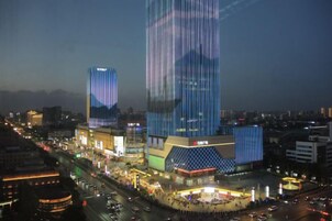 A high-rise building with a modern design, surrounded by a busy urban street with vehicles and illuminated signage.