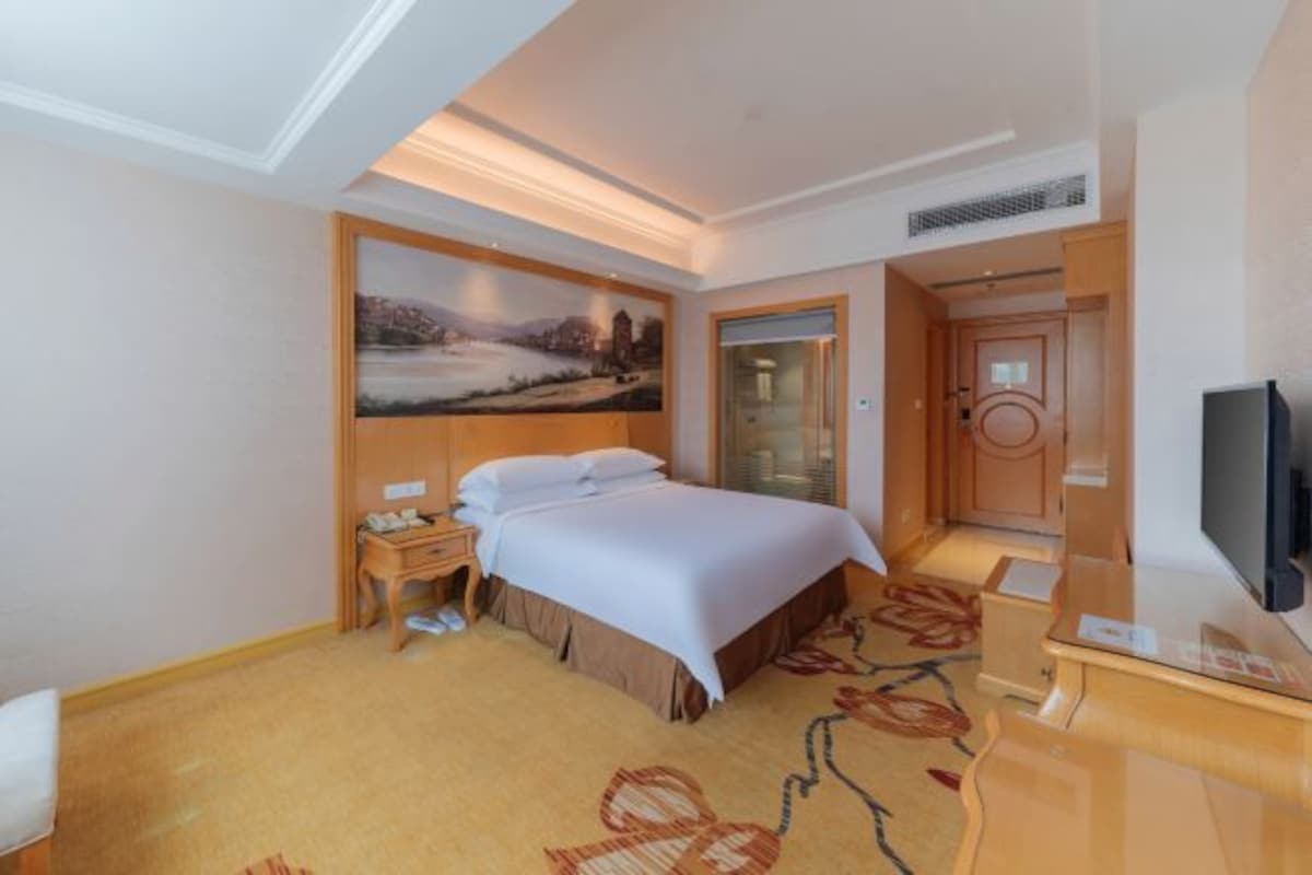 A hotel room with a bed, a television, a desk, and a painting on the wall.