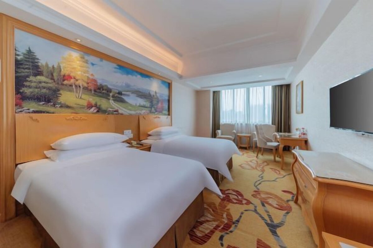 A hotel room with two beds, a painting on the wall, a desk, a chair, and a television.