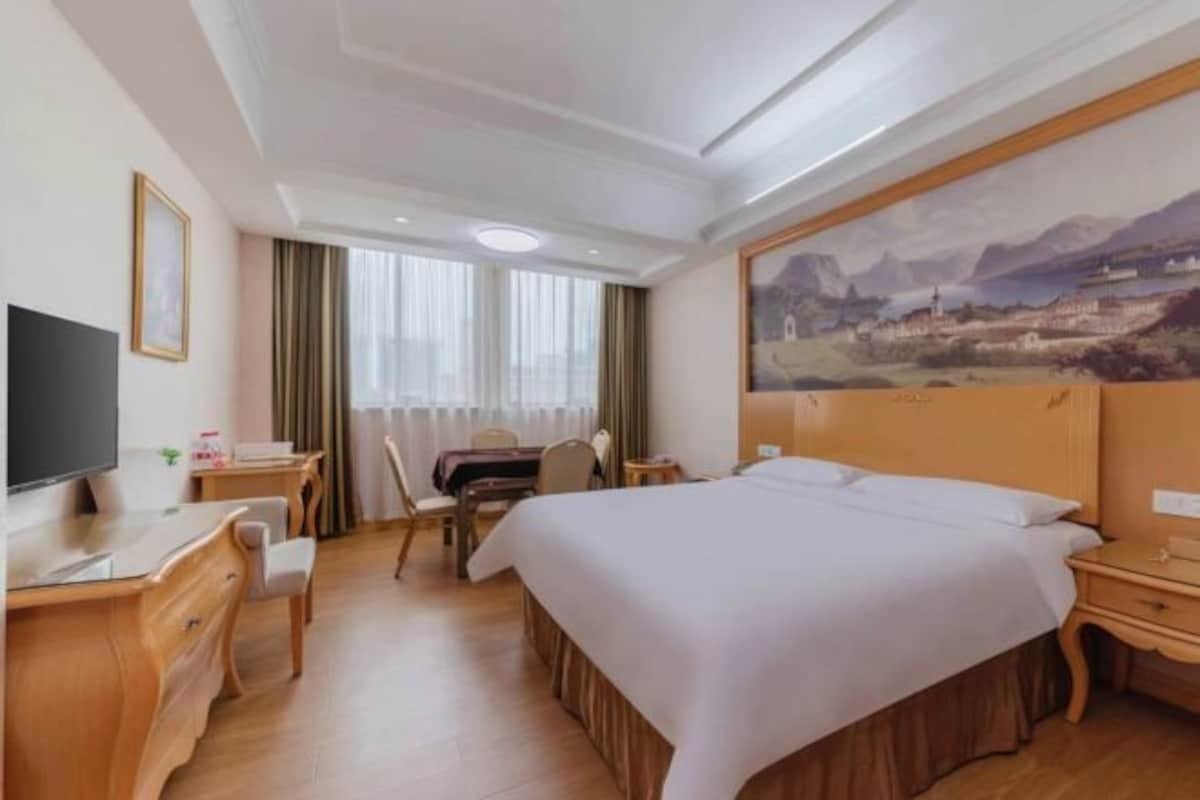 A hotel room with a large bed, a desk with a chair, a television, and a painting on the wall.
