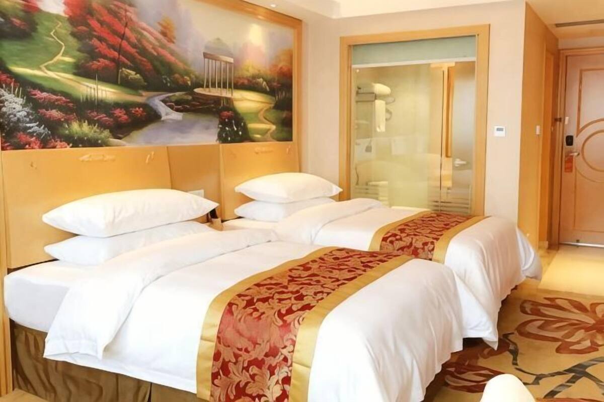 Ett hotellrum med två sängar, en målning som föreställer ett landskap, en glasdörr och ett golv täckt av matta.