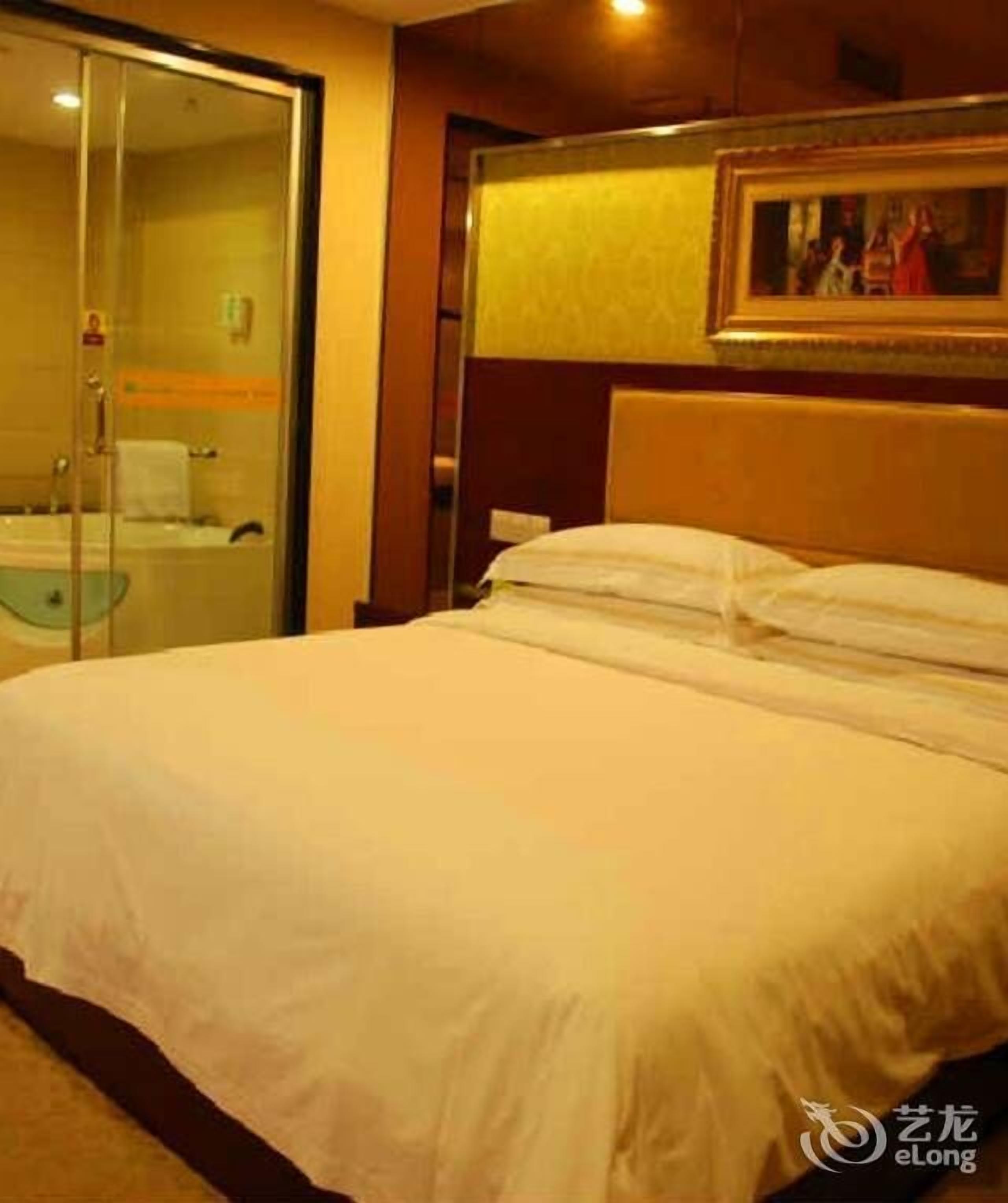 A hotel room with a bed, a glass shower enclosure, and a painting on the wall.