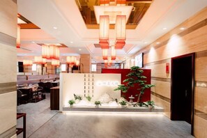 Un vestíbulo de hotel con mostrador de recepción, zona de estar y una planta grande.