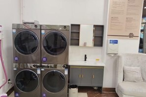 Un lavadero con lavadoras apiladas, un lavamanos y un armario.