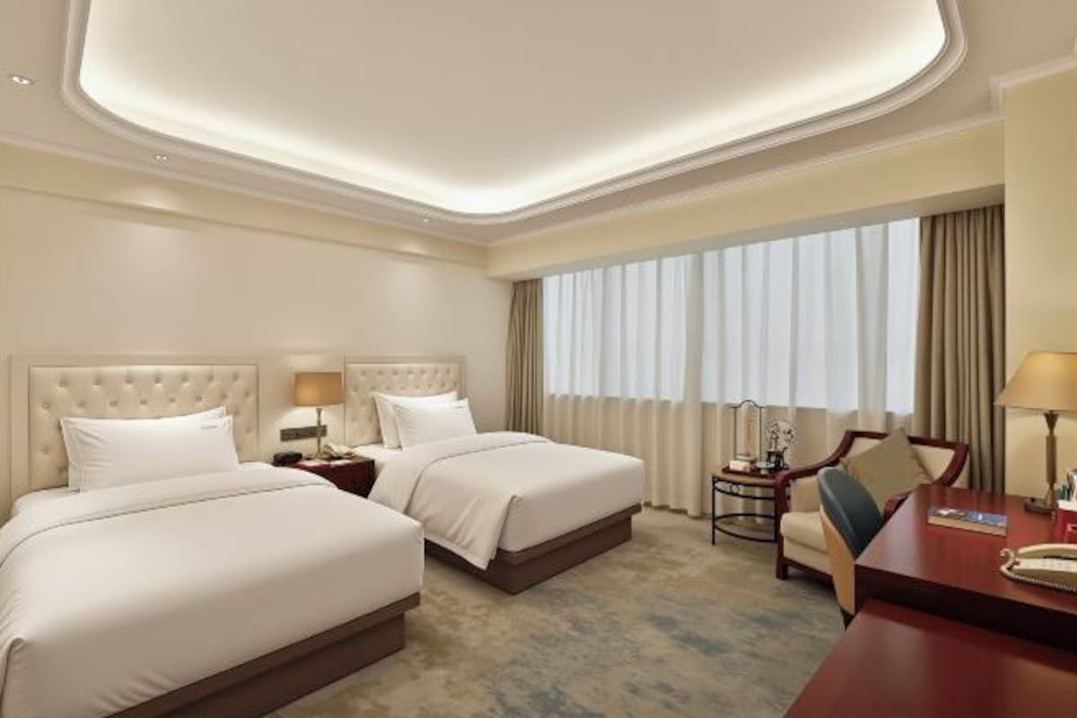 Habitación de hotel con dos camas, un escritorio, una silla y un ventanal con cortinas.