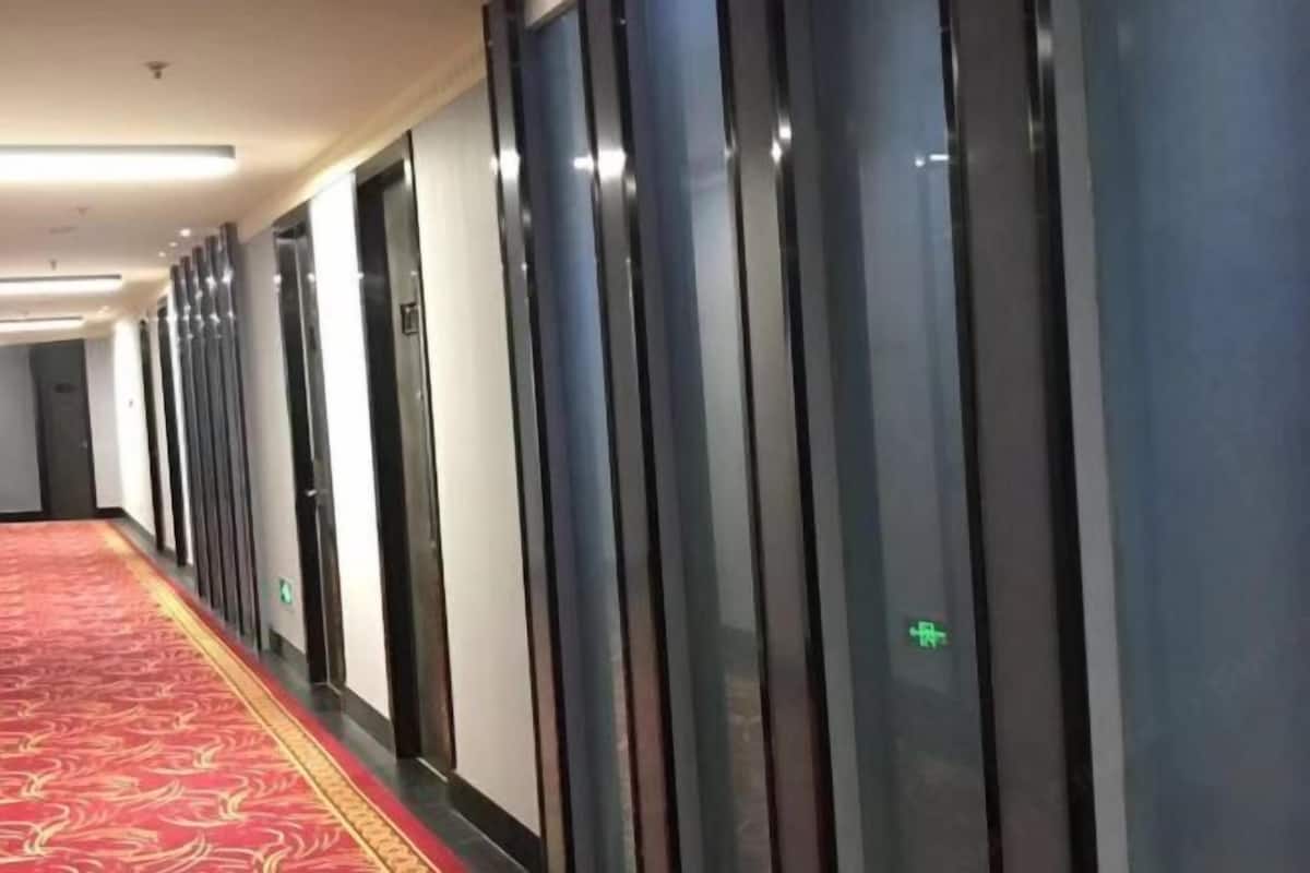 Un pasillo de hotel con alfombra roja, varias puertas y un ascensor de vidrio.