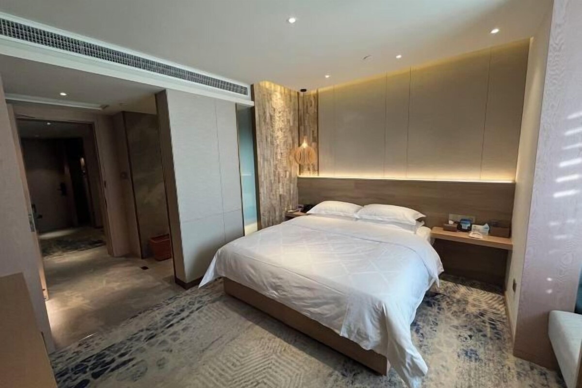 A modern hotel room with a large bed, a bedside table, and a built-in headboard.