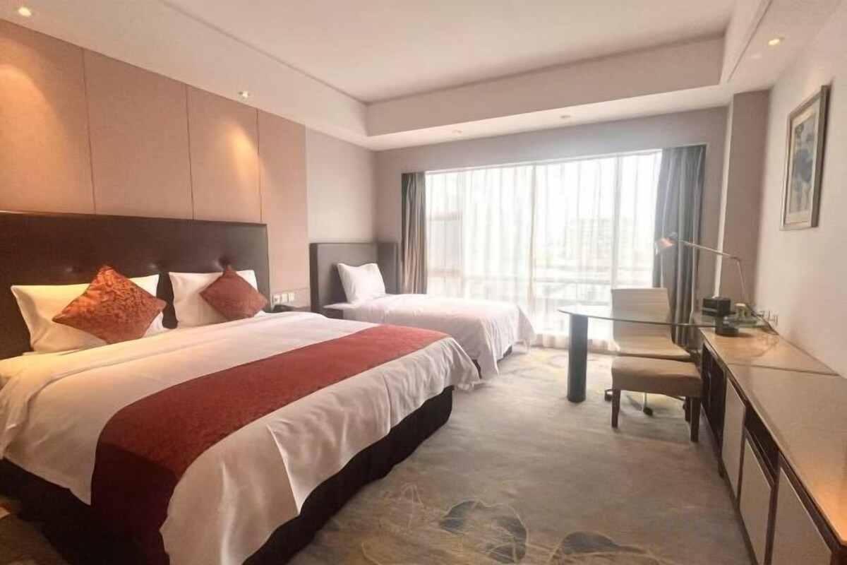 A hotel room with two beds, a desk, and a large window.