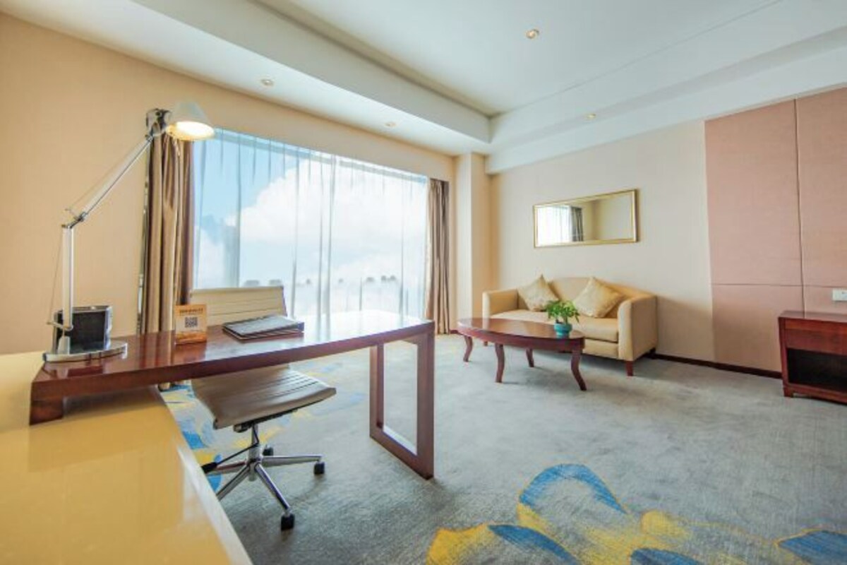 Habitación de hotel con escritorio, silla, sofá y un ventanal grande.