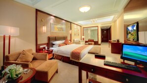Una habitación de hotel con una cama grande, un escritorio con ordenador, televisión y una zona de estar con sofá y sillones.