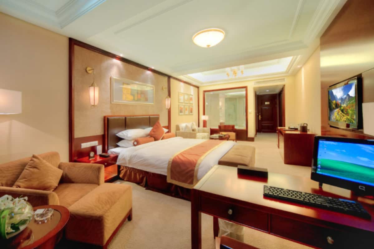 Une chambre d’hôtel dotée d’un grand lit, d’un bureau avec un ordinateur, d’une télévision et d’un coin salon comprenant un canapé et des fauteuils.
