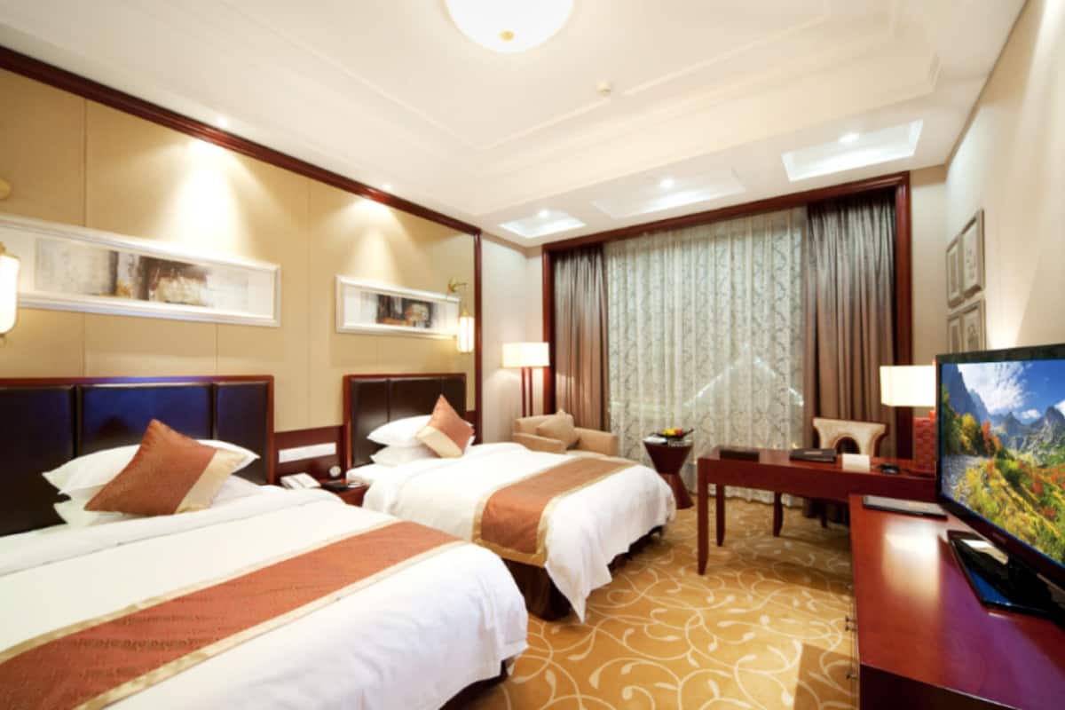 Une chambre d’hôtel avec deux lits, un bureau avec une télévision et une grande fenêtre avec des rideaux.
