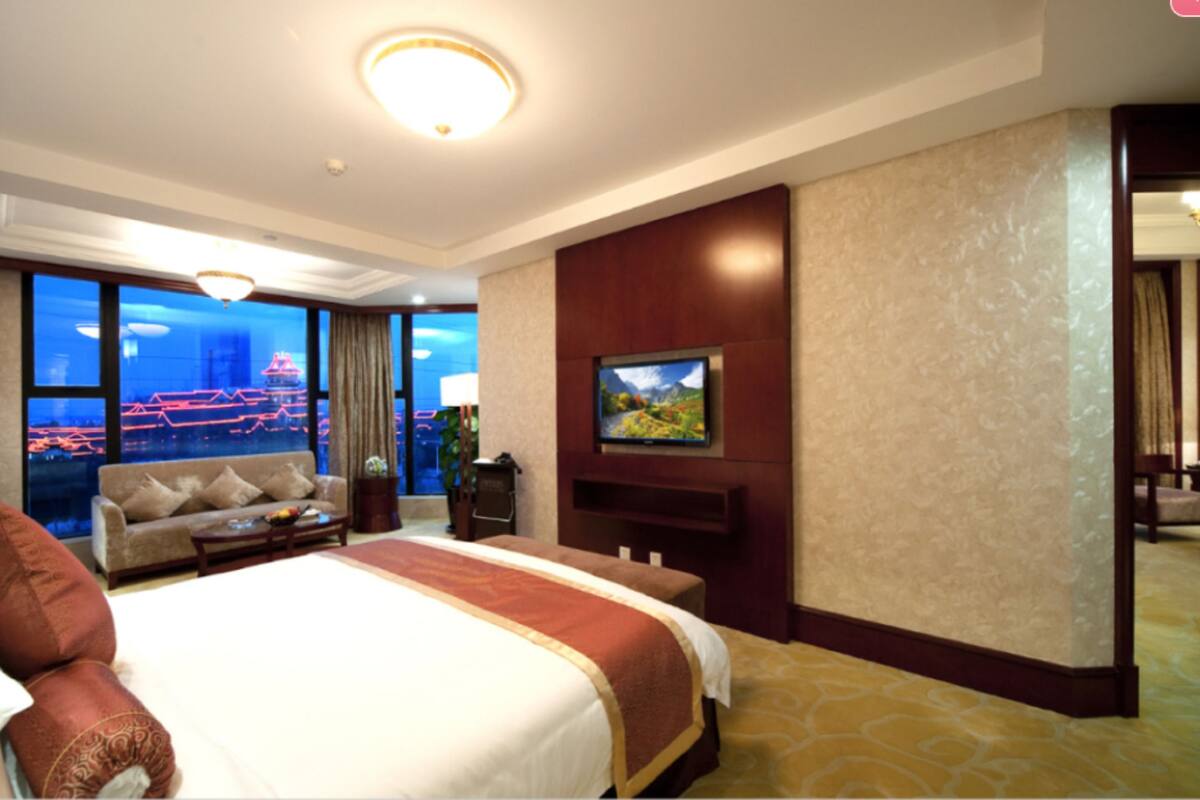 Une chambre d’hôtel dotée d’un grand lit, d’un canapé, d’un téléviseur fixé au mur et offrant une vue sur le paysage urbain grâce à de grandes fenêtres.