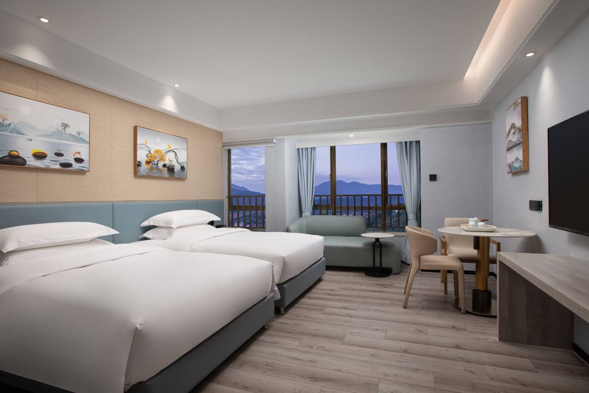 A hotel room with two beds, a sofa, a small table, and a TV.