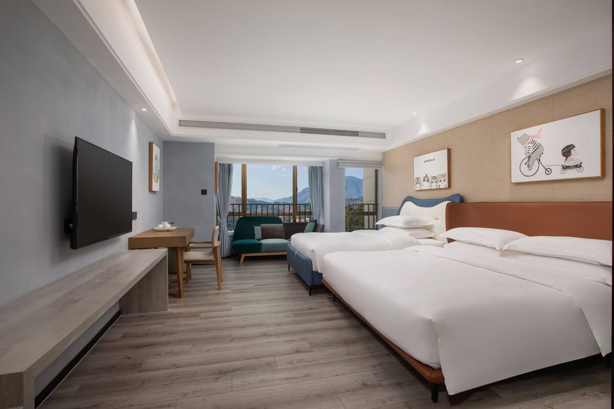 A modern hotel room with a large bed, a TV, a seating area with a sofa and chairs, and artwork on the walls.