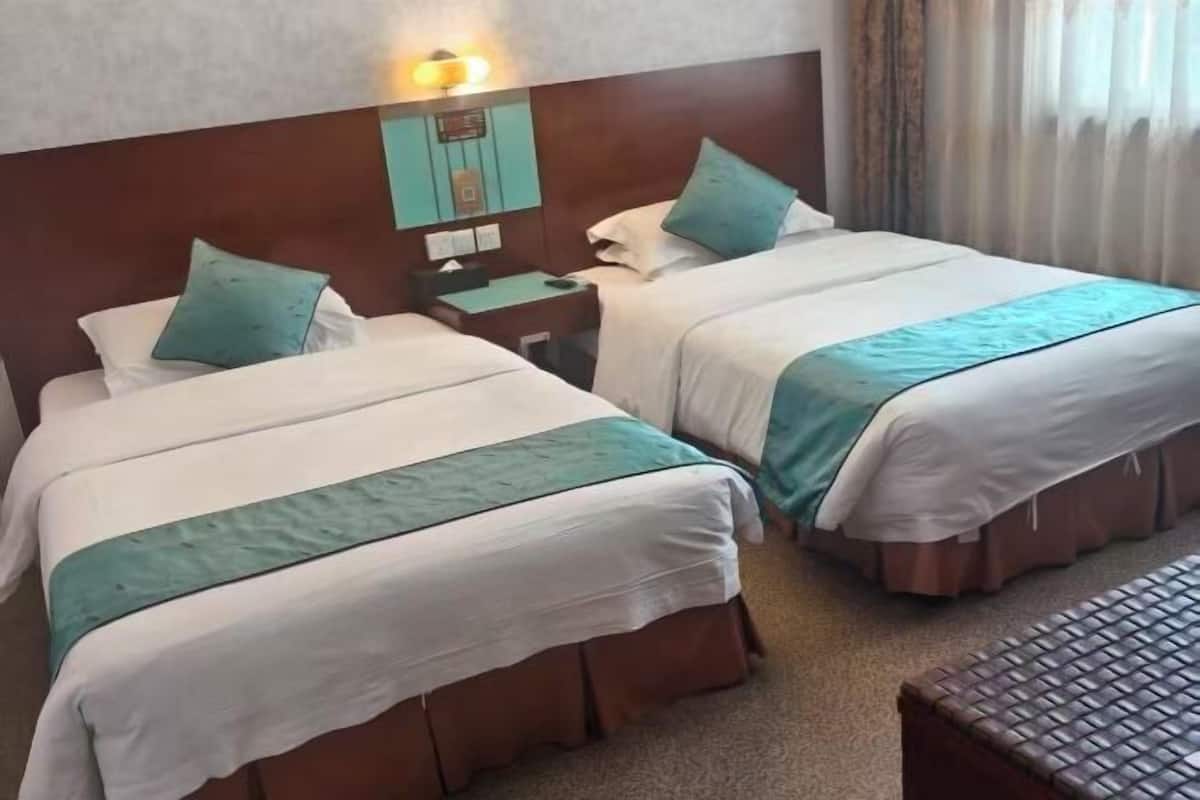 Een hotelkamer met twee bedden, een nachtkastje, een lamp en een raam met gordijnen.