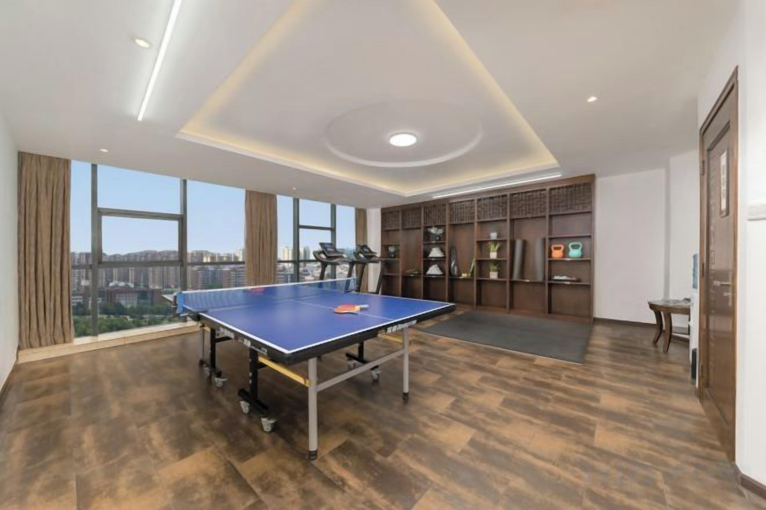 A room with a ping pong table, large windows, and a city view.