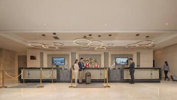 A hotel reception area with a modern design, featuring a reception desk, a trash bin, and a security barrier.