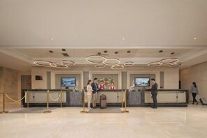 A hotel reception area with a modern design, featuring a reception desk, a trash bin, and a security barrier.