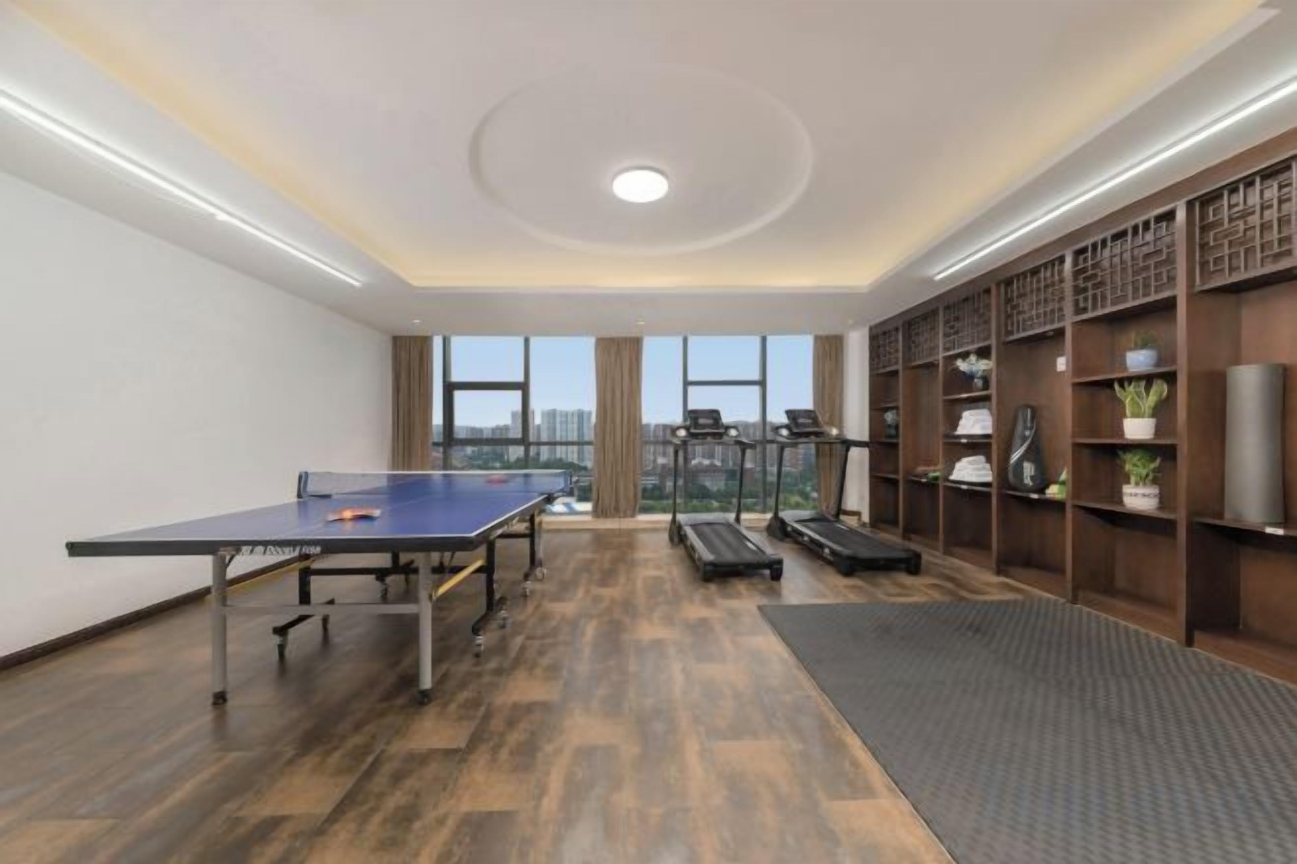 Une pièce équipée d’une table de ping-pong, de matériel d’exercice et d’une grande fenêtre donnant sur la ville.