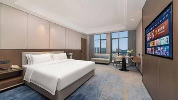 A modern hotel room with a large bed, a desk, and a view of the city.