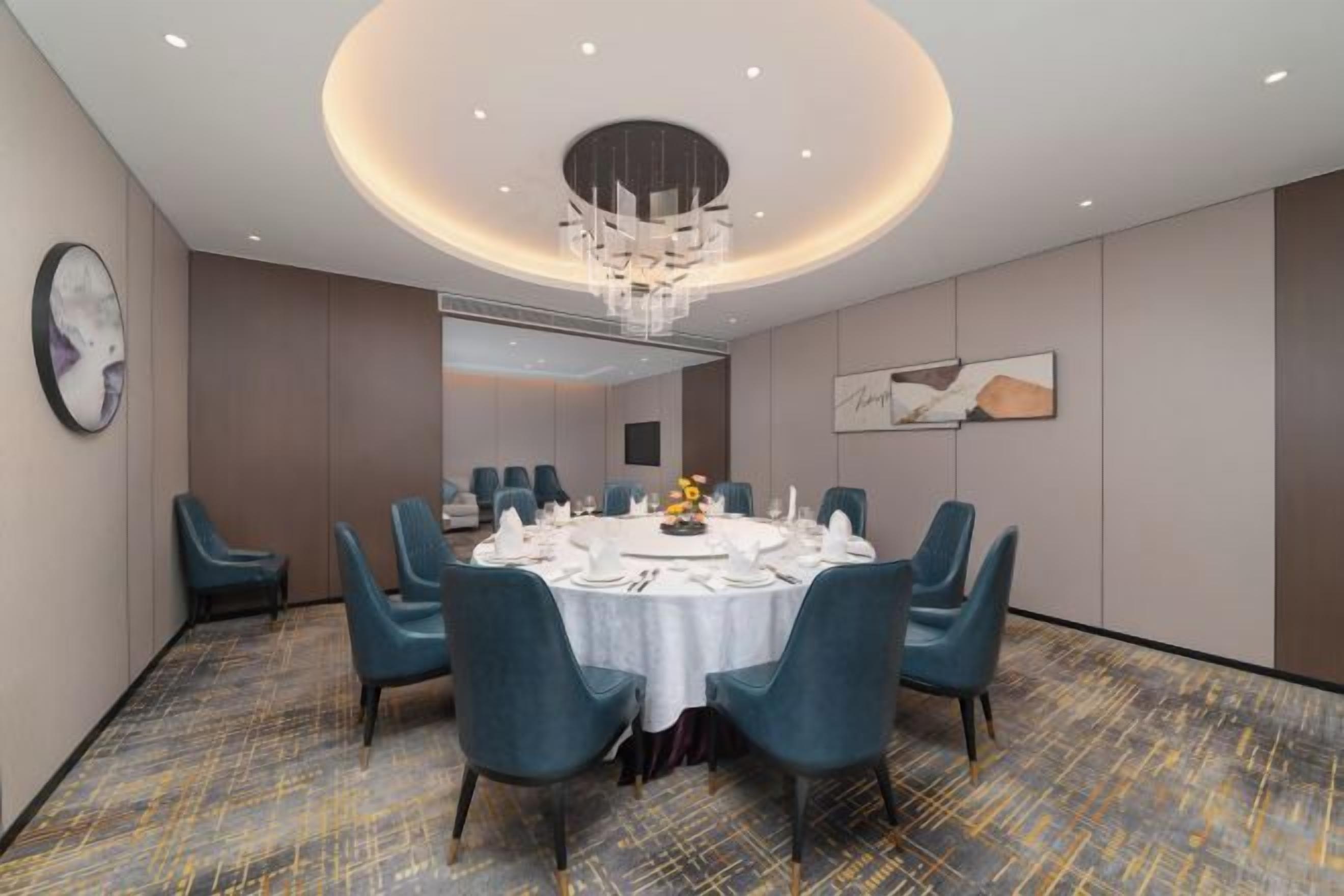 A conference room with a round table, blue chairs, and a chandelier.