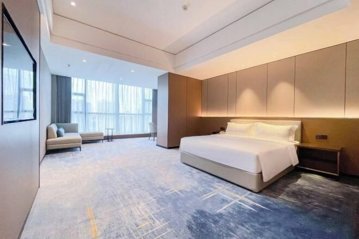 A modern hotel room with a large bed, a sofa, and a desk.