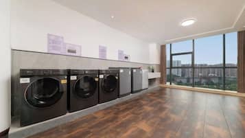 A laundry room with four washing machines, a large window with a city view, and a wooden floor.