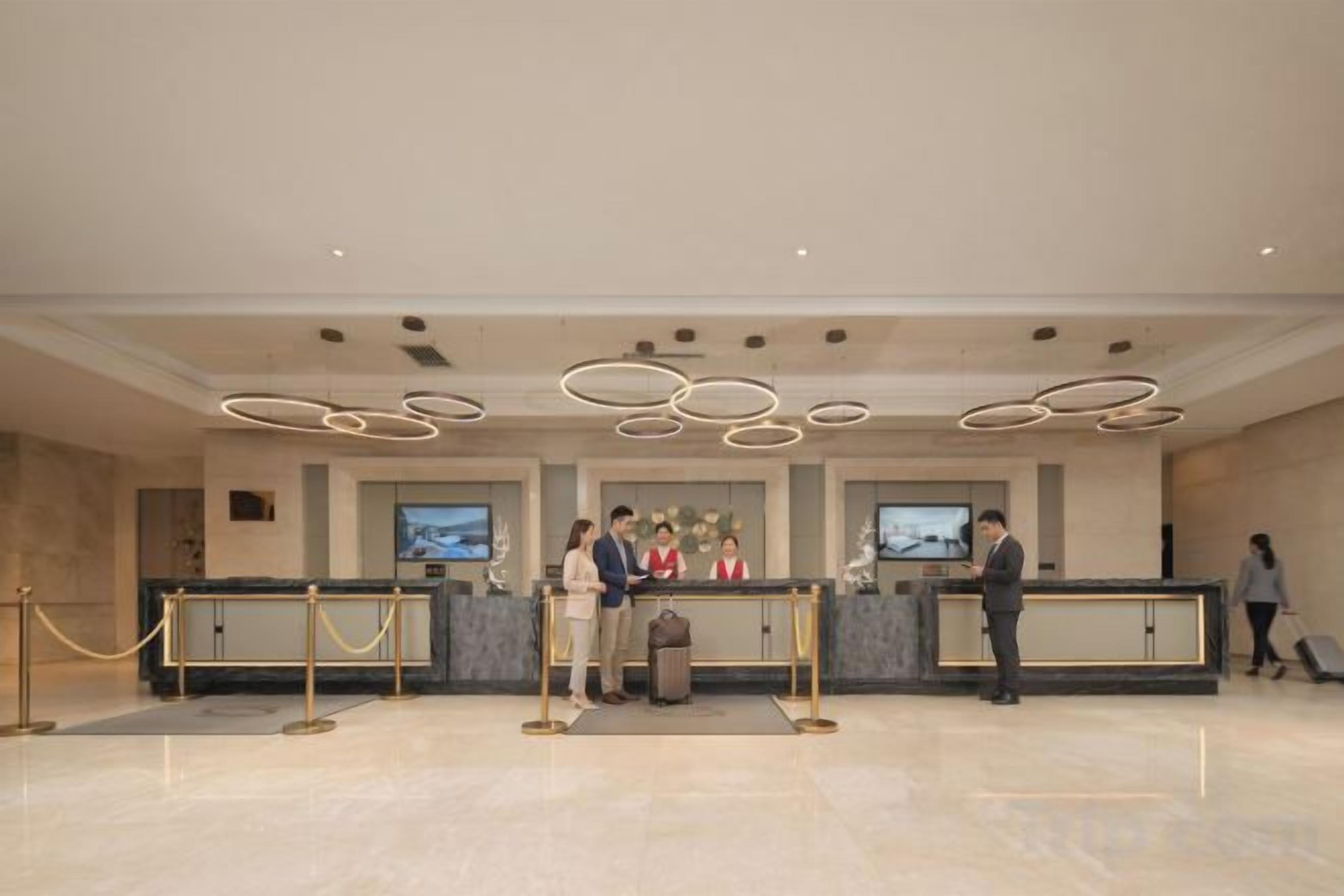 A hotel reception area with a modern design, featuring a reception desk, a television screen, and a seating area.