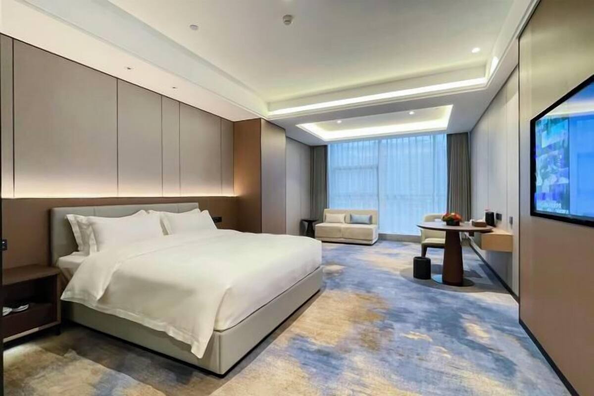 Quarto de hotel moderno com uma cama grande, um sofá, uma mesa pequena e uma televisão.