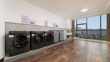 A laundry room with four washing machines, a wooden floor, and large windows offering a city view.