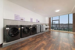 A laundry room with four washing machines, a wooden floor, and large windows offering a city view. - Sylva Hotel (Changsha)