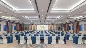 A conference room with rows of tables and chairs, a presentation screen, and a carpeted floor.