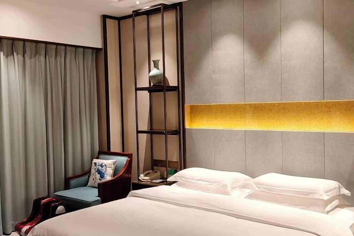 A hotel room with a bed, a nightstand, a chair, a decorative shelf, and a curtain.