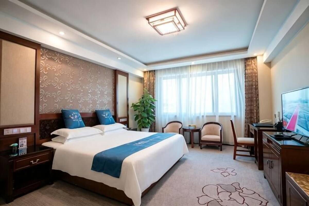 A hotel room with a large bed, a desk with a computer, a chair, a TV, and a window with curtains.