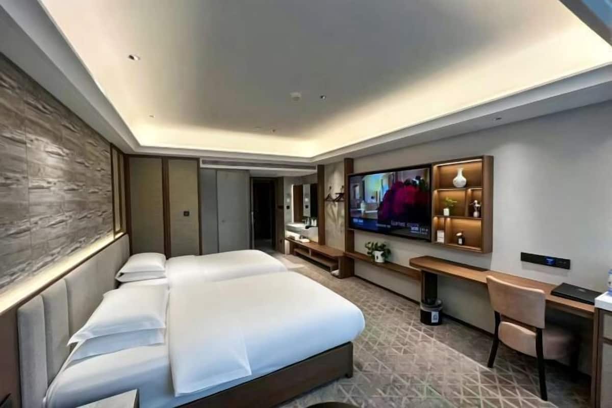A hotel room with a large bed, a desk, a TV, and a mirror.
