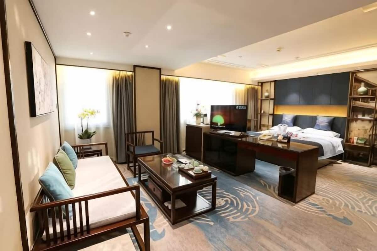 A hotel room with a bed, a desk, a television, a sofa, and a dining table.