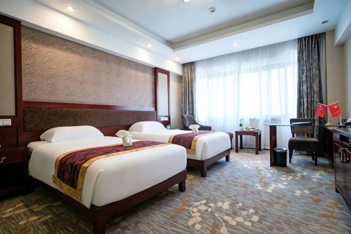 A hotel room with two beds, a desk, a chair, and a large window with curtains.