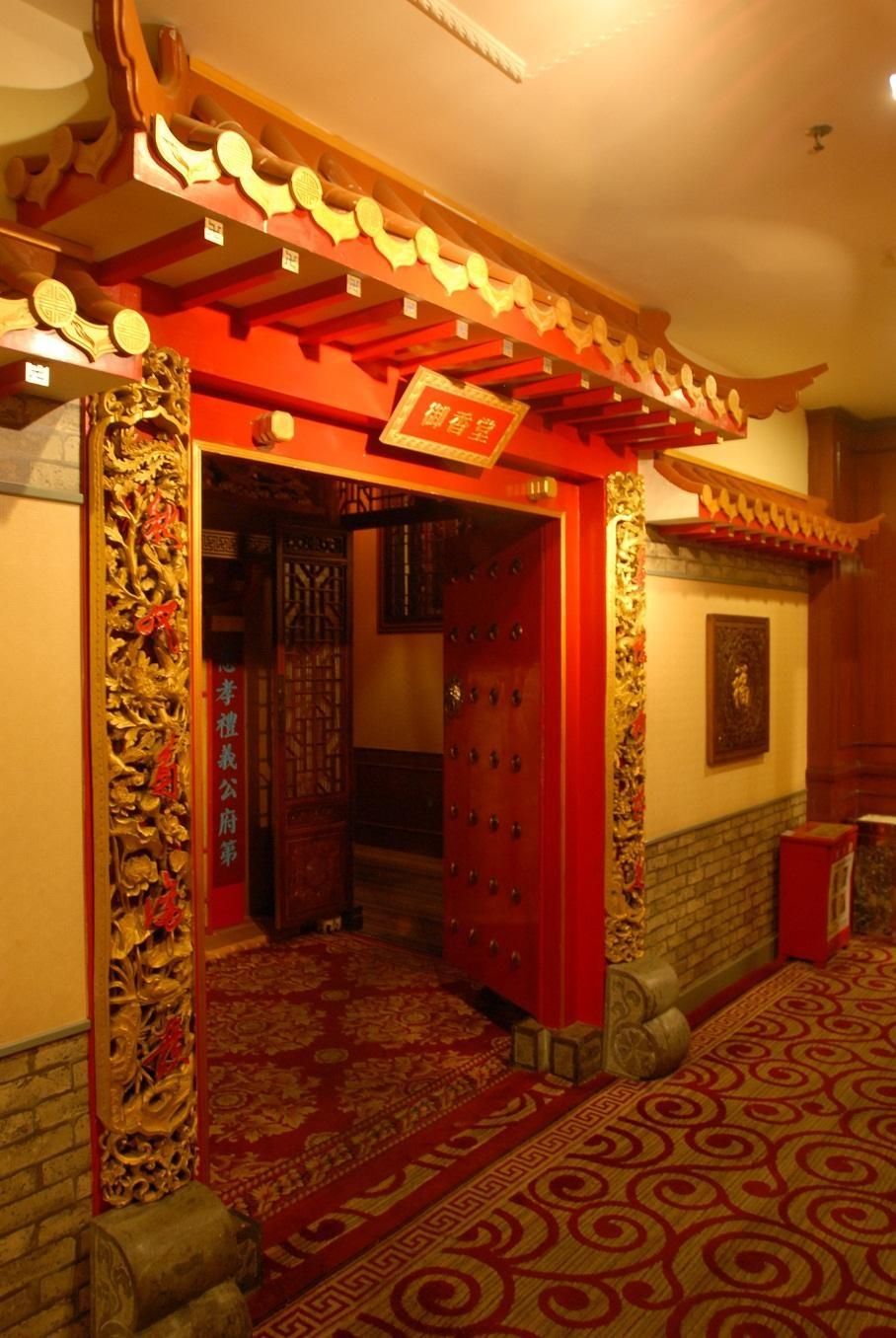 Una entrada arquitectónica tradicional china con decoraciones elaboradas, una puerta roja y una alfombra estampada.