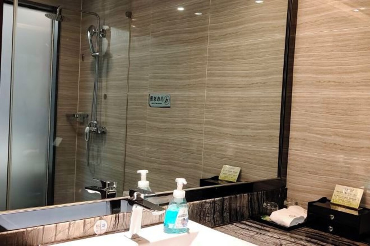Un baño moderno con ducha envuelta en vidrio, un espejo grande y un mueble de tocador con dispensadores de jabón.
