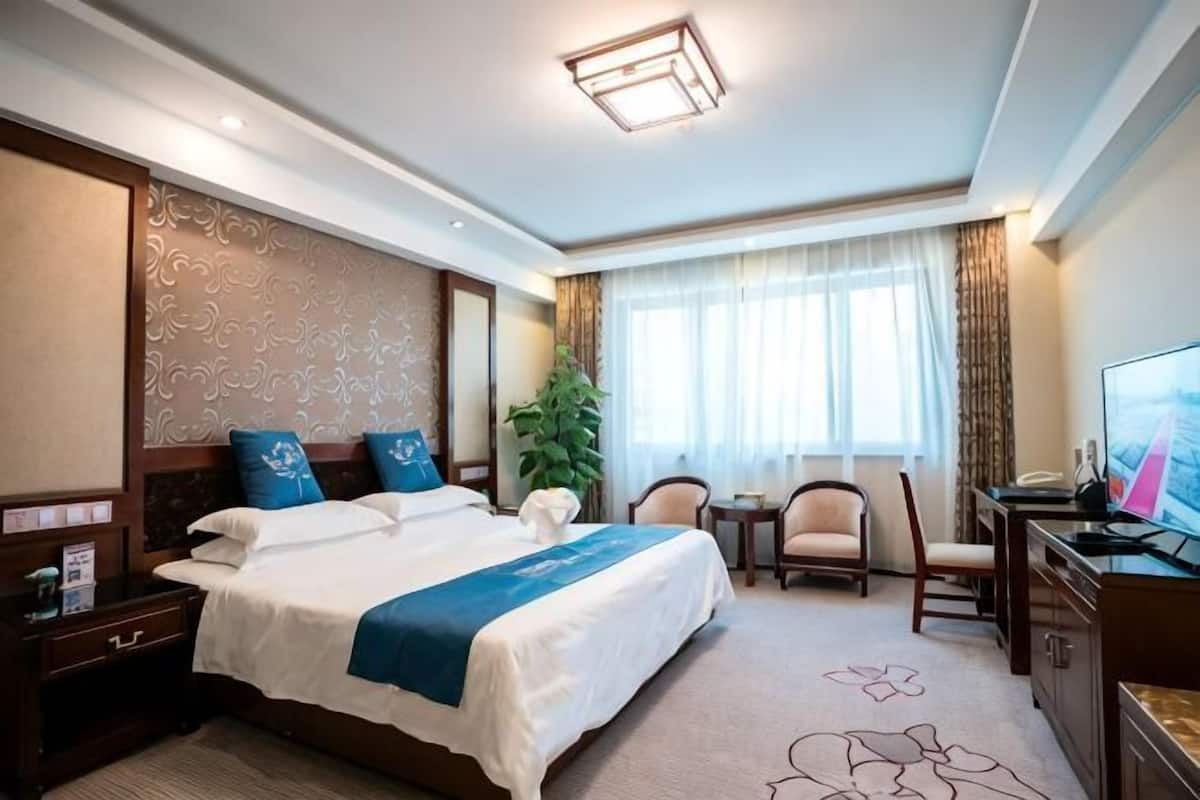 A hotel room with a large bed, a desk, a chair, a television, and a window with curtains.