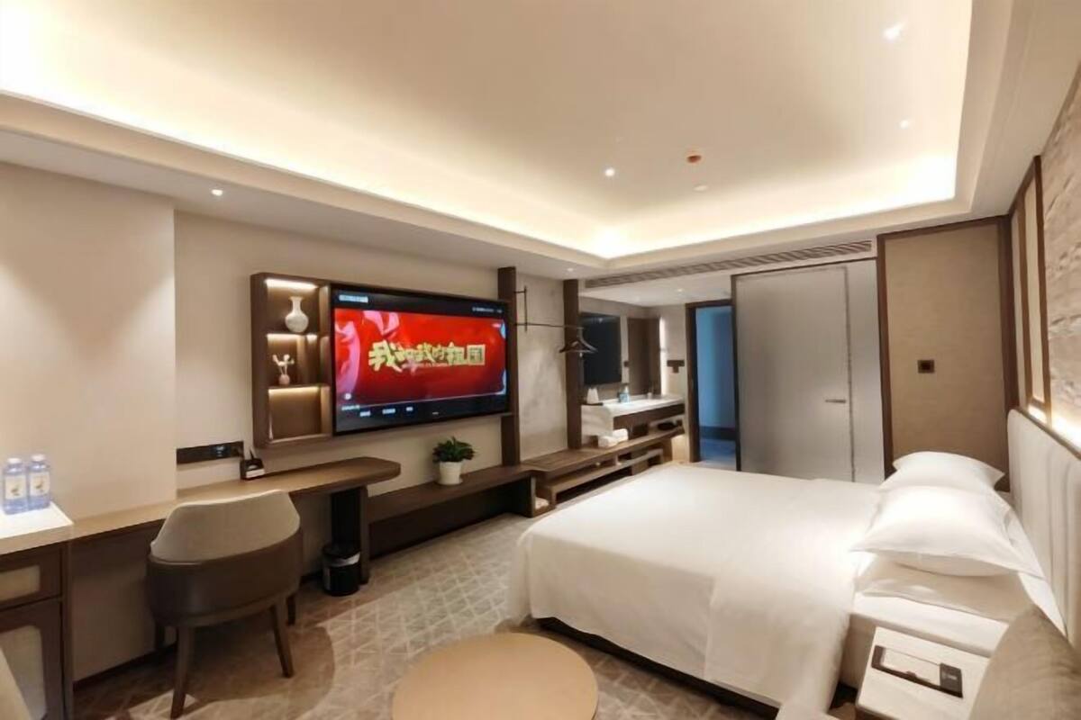 A modern hotel room with a bed, desk, chair, TV, and a wardrobe.