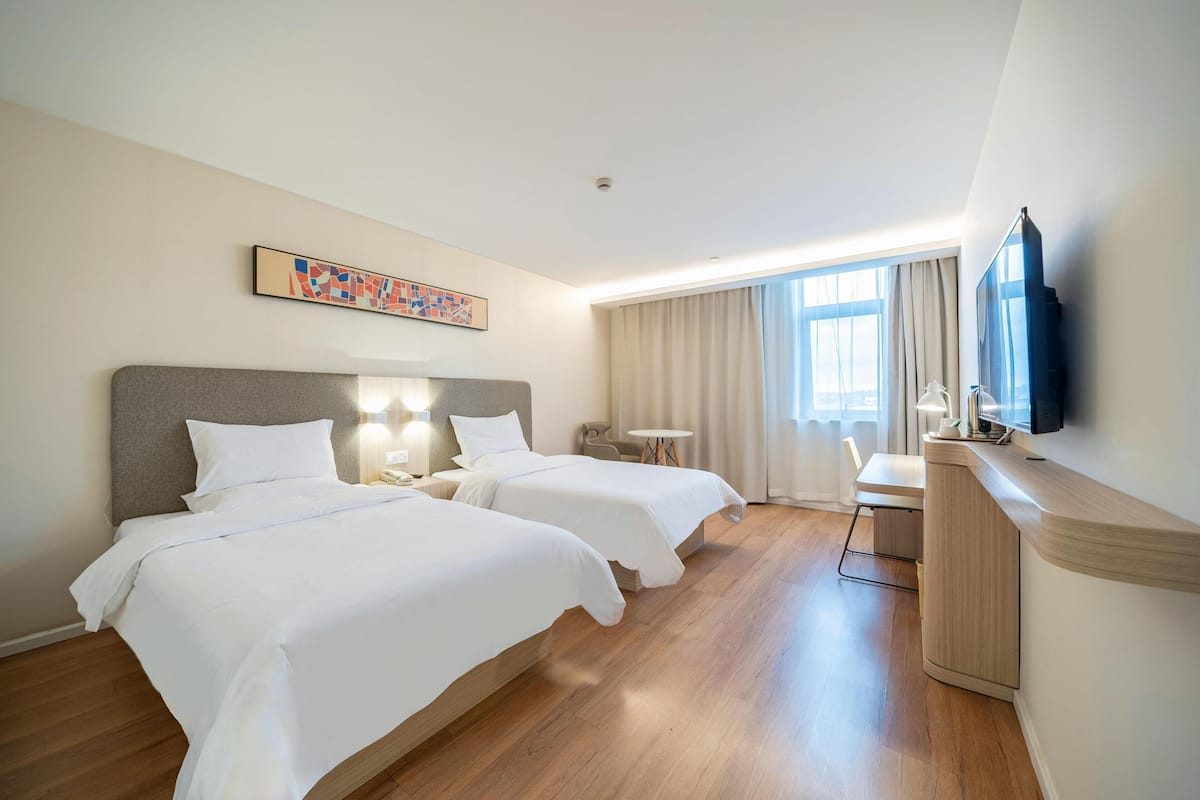 Une chambre d’hôtel avec deux lits, un bureau, une chaise, une télévision et une fenêtre avec des rideaux.