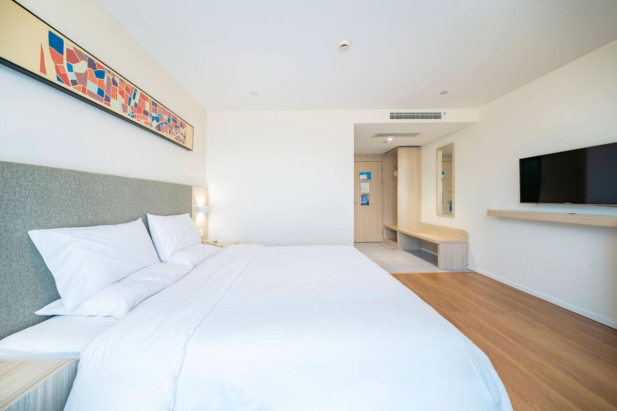 Une chambre d’hôtel moderne avec un grand lit, un téléviseur à écran plat, un tableau au mur et un banc en bois.