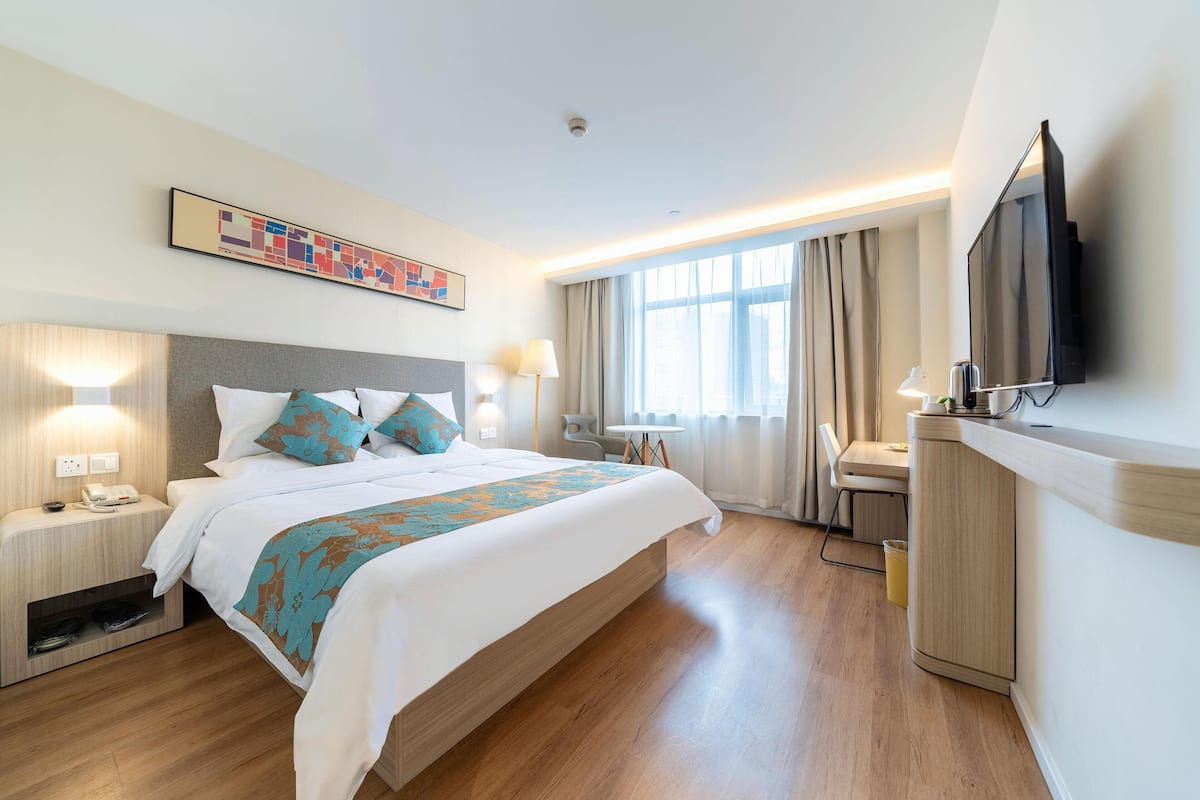 Une chambre d’hôtel avec un lit, des tables de chevet, un bureau, une télévision et une fenêtre avec des rideaux.