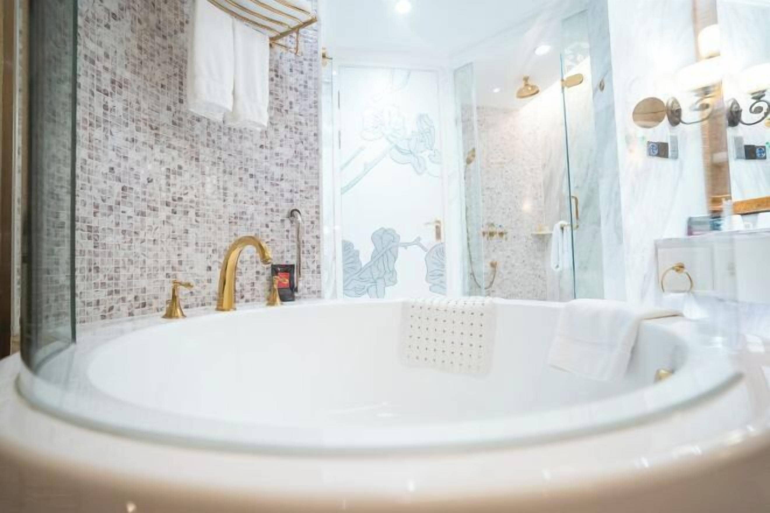 Un baño con una bañera grande, un grifo dorado y una pared de azulejos.