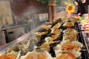 A row of oysters on a grill with a kitchen in the background. - Sun Lake Hotel (Jiaxing)