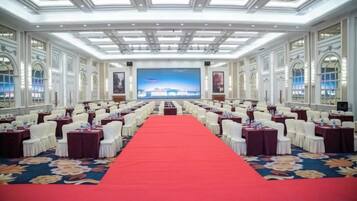 A conference room with rows of tables and chairs, a red carpet, and a large screen at the front.