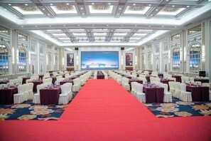 Un salón de conferencias con filas de mesas y sillas, una alfombra roja y una pantalla grande al frente.
